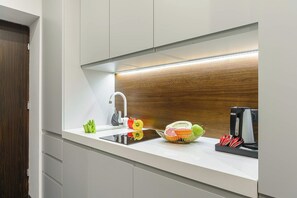 Eine moderne Küche mit integriertem Spülbecken, einer Holz-Spritzschutzwand und einer Arbeitsplatte mit Obstschale, Wasserkocher und Kaffeemaschine.