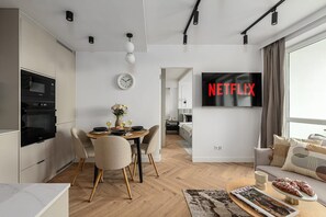 A modern living space with a dining area, kitchen, and a TV displaying 'NETFLIX'. - Elegant Family Apartment in Nowolipki (Warszawa 2)