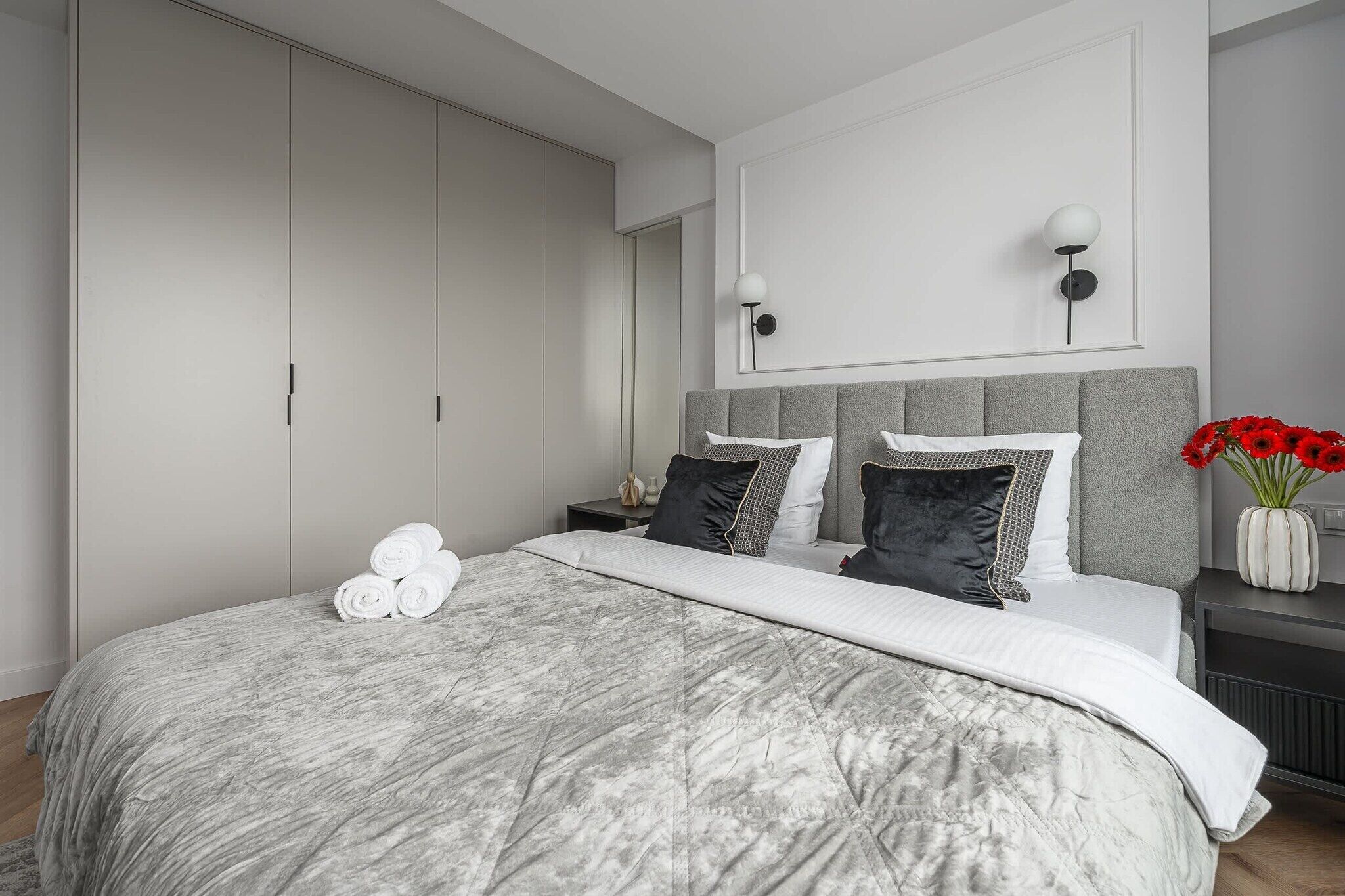 Een slaapkamer met een groot bed, een grijs hoofdeinde en een kledingkast.