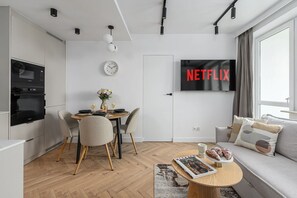 Un salon moderne comprenant un coin repas, un téléviseur à écran plat diffusant du contenu de « NETFLIX », et un espace détente confortable avec un canapé et une table basse.