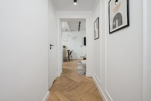 A hallway with a wooden floor leading to a dining area with a table and chairs. - Elegant Family Apartment in Nowolipki (Warszawa 2)