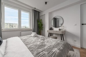 A bedroom with a large bed, a bedside table with a mirror, a radiator, and a window with curtains. - Elegant Family Apartment in Nowolipki (Warszawa 2)