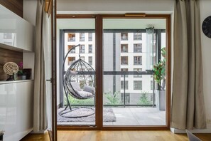 Een kamer met een schuifdeur die leidt naar een balkon, een hangstoel en een pot met een plant.