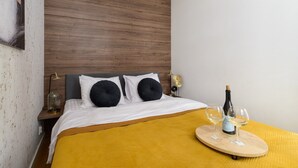 Ett hotellrum med en säng, ett träfärgat sänggavel, två sängbord med lampor, en gul pläd och ett brickbord med en flaska och glas.