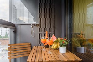 A wooden table with two glasses of orange juice and a bottle of champagne, a potted plant with red flowers, and a metal mesh wall in the background. - City Apartment with Balcony (Warszawa)