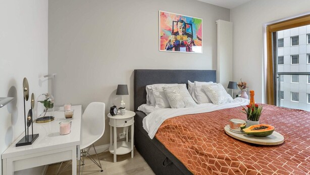 A modern hotel room with a large bed, a desk, and a window with a city view. - City Apartment with Balcony (Warszawa)