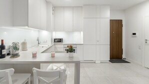 A modern kitchen with white cabinetry, a central island, and a wooden door. - City Apartment with Balcony (Warszawa)