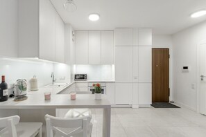 A modern kitchen with white cabinetry, a central island, and a wooden door. - City Apartment with Balcony (Warszawa)