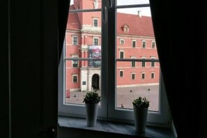 Ein Fenster mit zwei Blumentöpfen, Blick auf ein Gebäude mit roter Fassade und einem Rundbogen.
