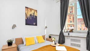 A modern bedroom with a bed, bedside tables, a nightstand, a window with curtains, and a cityscape painting on the wall. - Comfortable house with splendid sea view (Warszawa)