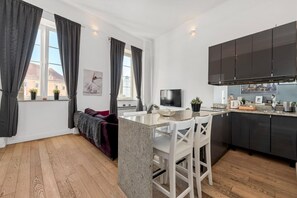 Een moderne keuken met donkere kastjes, een marmeren aanrechtblad en een bar met witte stoelen.