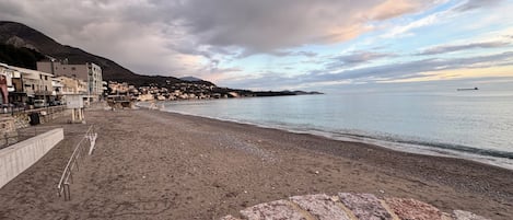 A coastal beach with a stone wall, a clear sky, and a distant view of a town.