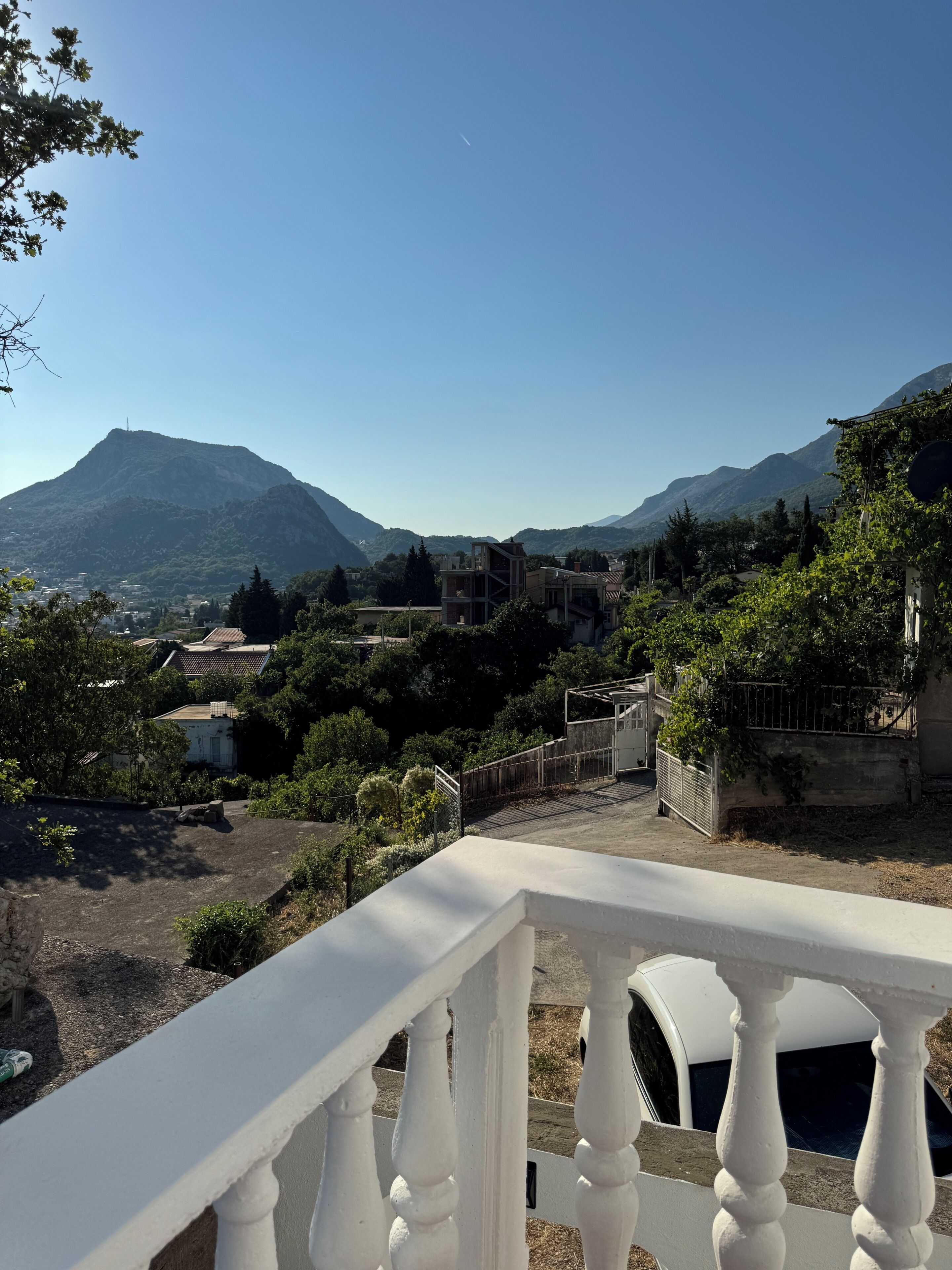Ein Balkon mit Blick auf eine gebirgige Landschaft, einem weißen Zaun und einem parkenden Auto.