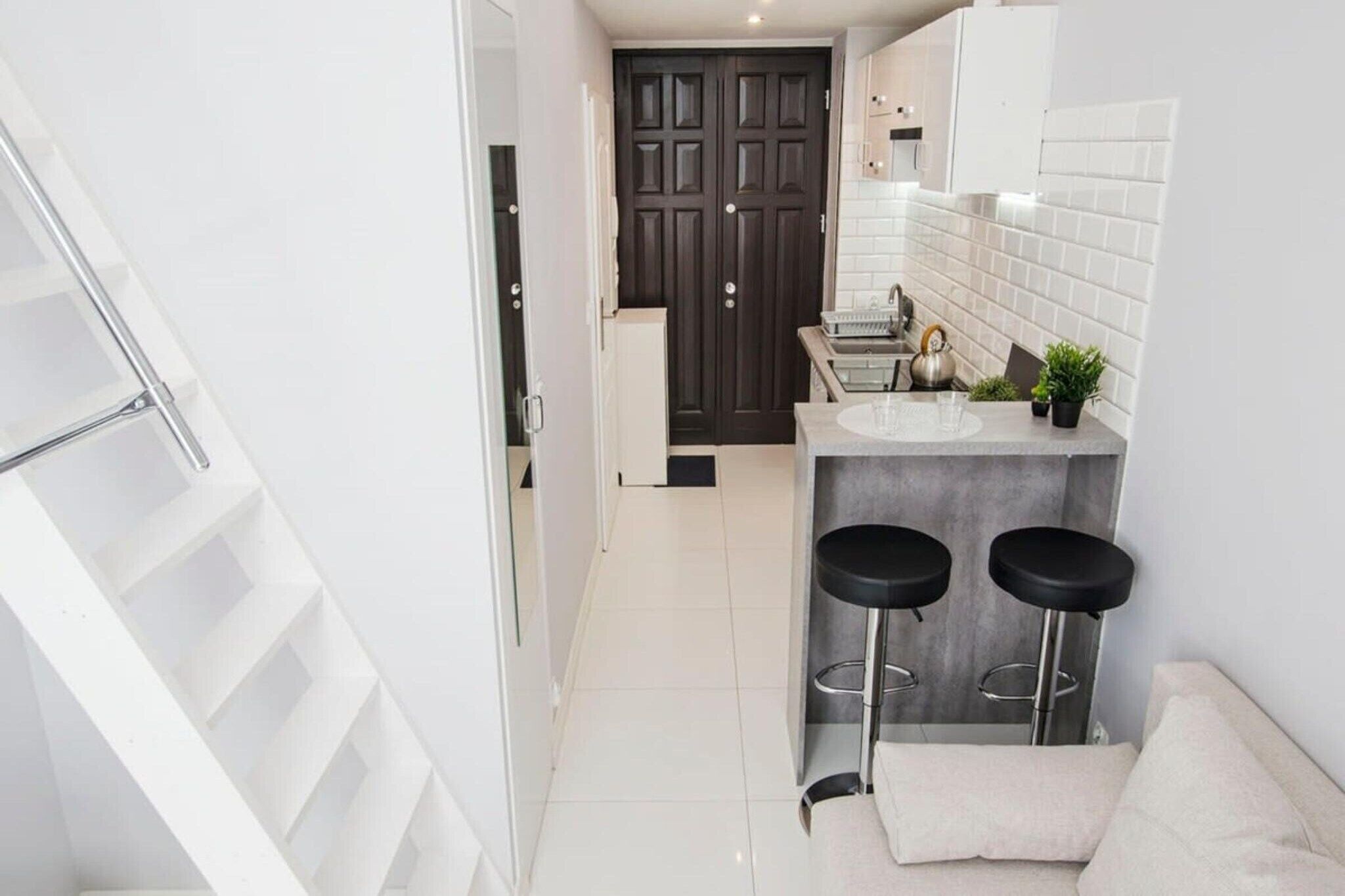 A modern kitchen with a dark door, white tiles, and two black bar stools.