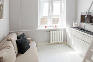 Ein modernes Wohnzimmer mit Sofa, Heizkörper, einem Fenster und zwei roten Tassen sowie einem Fernseher auf einem Schrank.