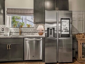 A modern kitchen with stainless steel appliances, a built-in dishwasher, and a window with potted plants.