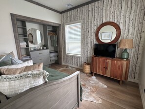 Ein Schlafzimmer mit Bett, Kleiderschrank, Fernseher und einem Fenster mit Jalousien.