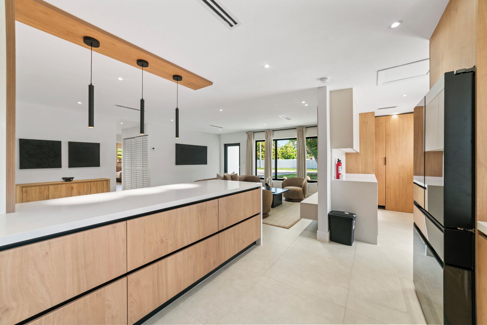 A modern kitchen with a large island, wooden cabinets, and pendant lighting.
