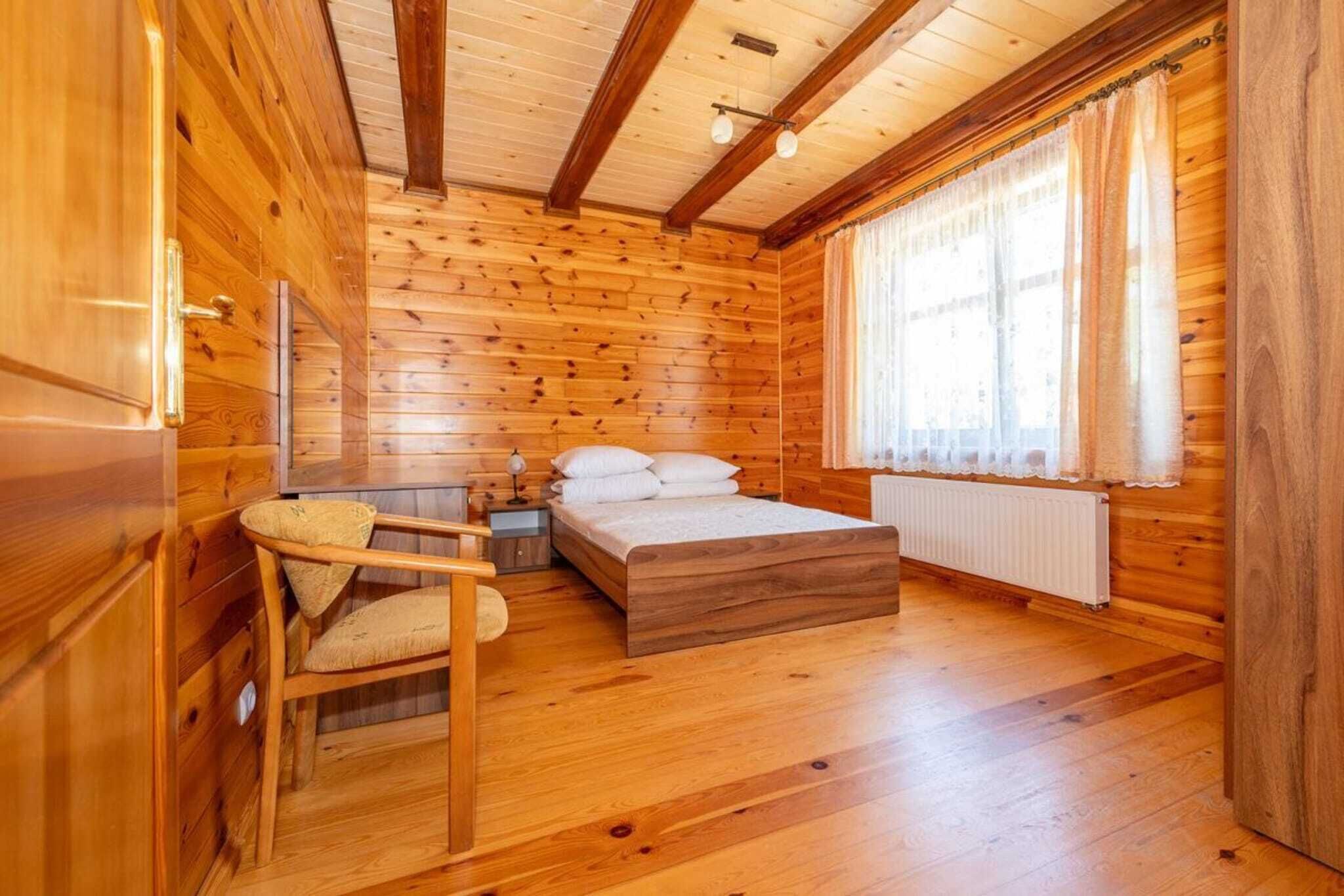 A wooden cabin room with a bed, a chair, and a window with curtains.