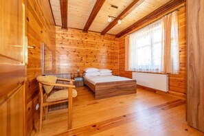 A wooden cabin room with a bed, a chair, and a window with curtains. - Comfortable holiday home with a fireplace (Bobolin)