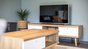 Un soggiorno moderno con una televisione a schermo piatto montata a parete, un tavolino in legno, un mobiletto bianco e una pianta in vaso.