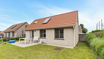 Une maison d’habitation avec un toit en tuiles, un petit patio avec une table et des chaises, et une cour gazonnée.
