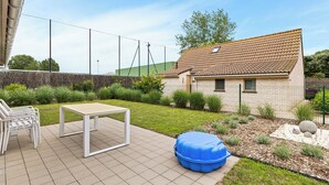 Un'area patio con tavolo e sedie, un sacco di spugna blu e una piccola casa con tetto in tegole.
