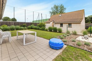 Eine Terrasse mit Tisch und Stühlen, einem blauen Sitzsack und einem kleinen Haus mit einem Ziegeldach.