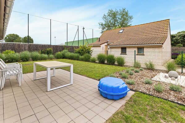 Un espace patio avec une table et des chaises, un fauteuil poire bleu et une petite maison avec un toit en tuiles.