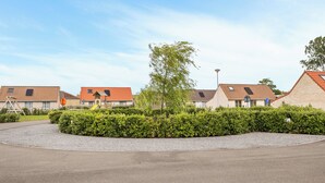 Un quartiere residenziale con diverse case, uno spazio centrale curato con siepi e un cielo sereno.