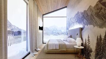 A bedroom with a large window, a bed, a nightstand, and a wall mural of a mountainous landscape.