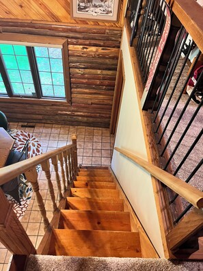 Eine Holztreppe mit Handlauf, die zu einem Zimmer mit Fenster und einem gemusterten Teppich führt.