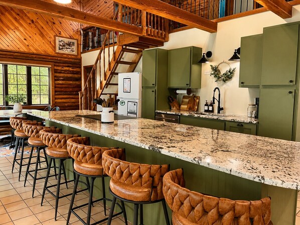 Una cocina con una isla alargada, taburetes de bar y una escalera que sube a un nivel superior.