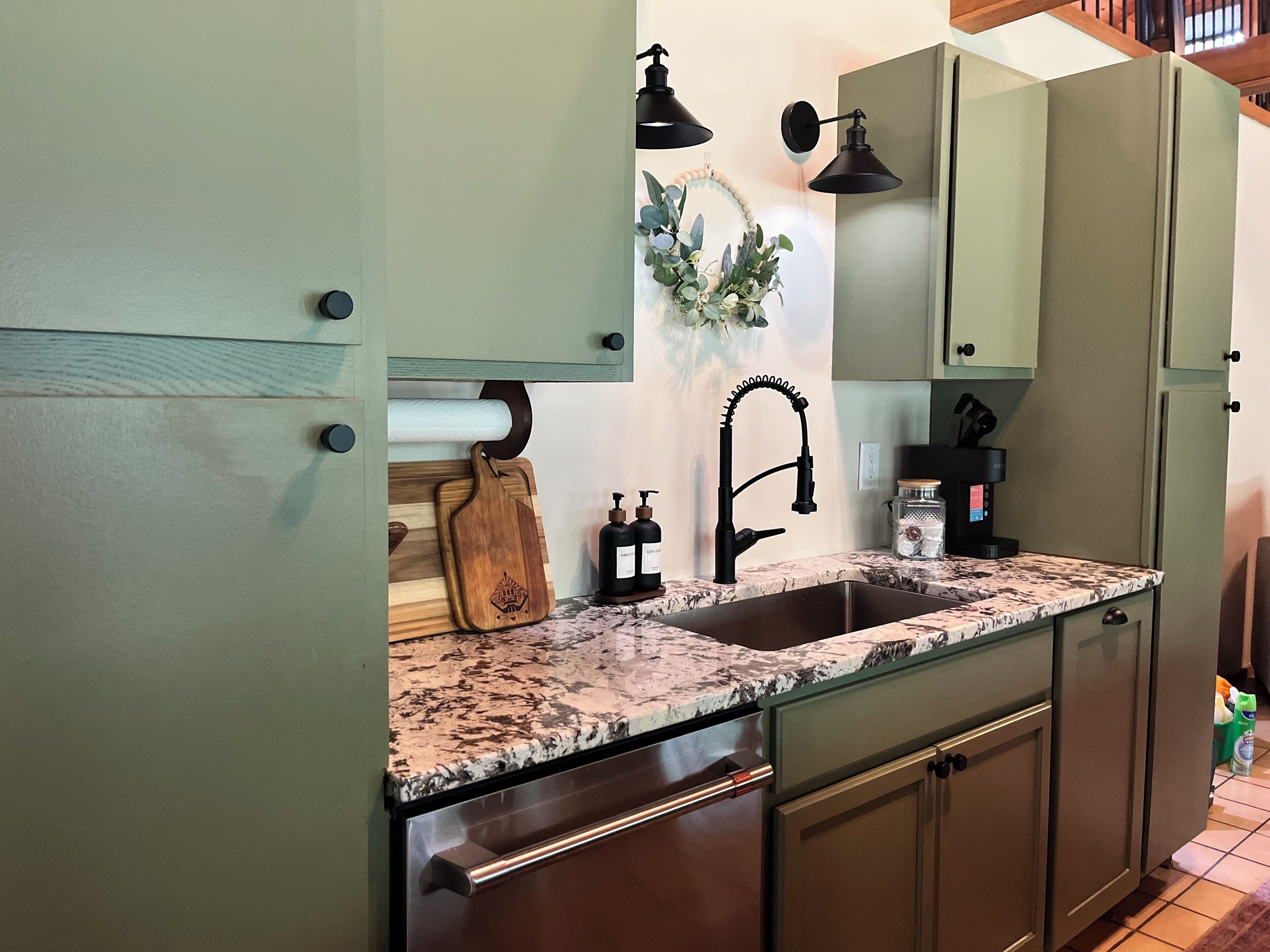 A kitchen with a granite countertop, a stainless steel sink, a wooden cutting board, a black faucet, and a coffee maker.