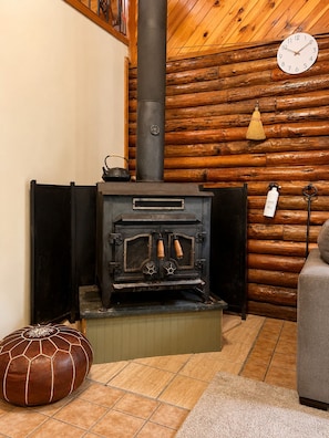 Ein Holzblockhaus-Interieur mit Kaminofen, einer Wanduhr und einem Sofa.