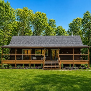 Eine Holzblockhütte mit Veranda, Schornstein und Blick auf den umliegenden Wald.