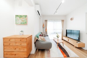A modern living room with a sofa, a wooden cabinet, a flat-screen TV, and a large window with curtains. - Toka Art Hotel (Taito)
