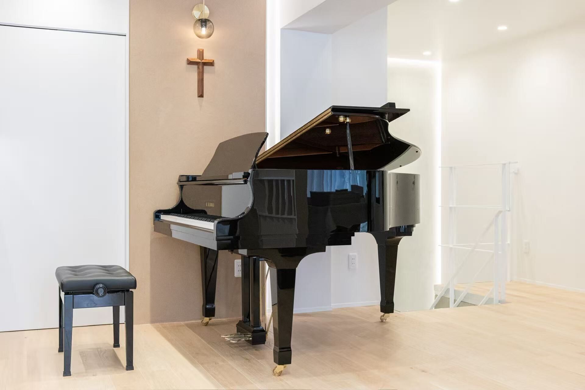 Un piano à queue dans une pièce moderne, avec une croix en bois accrochée au mur, un banc de piano et un luminaire.