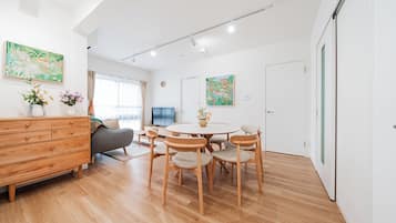A modern living room with a wooden dresser, a grey sofa, a round dining table with chairs, and two large paintings on the walls.