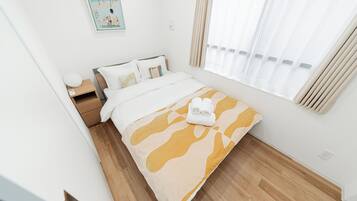 A hotel room with a bed, a nightstand, a lamp, a window with curtains, and a painting on the wall.