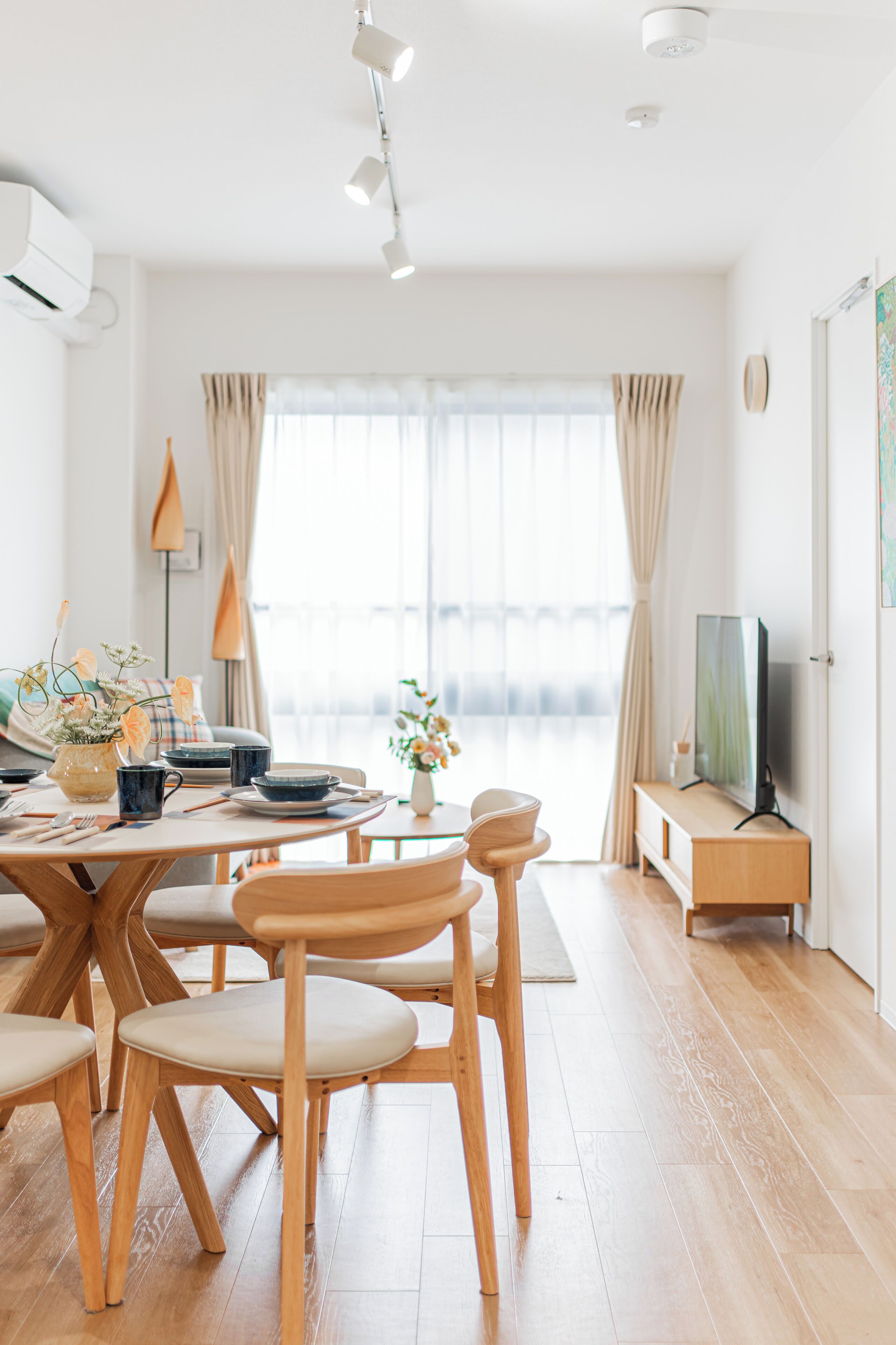 Un salon moderne comprenant un coin repas, des meubles en bois, un téléviseur à écran plat et une grande fenêtre avec des rideaux.