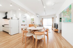 Eine moderne Küche mit weißen Geräten, ein Essbereich mit Holzstühlen und ein großes Fenster mit Vorhängen.