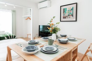 A neatly arranged dining area with a table set for four, a television, and a framed artwork on the wall. - Toka Art Hotel (Taito)