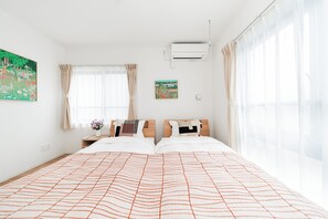 A hotel room with a large bed, a bedside table with a vase of flowers, a wall-mounted air conditioner, and a window with sheer curtains. - Toka Art Hotel (Taito)