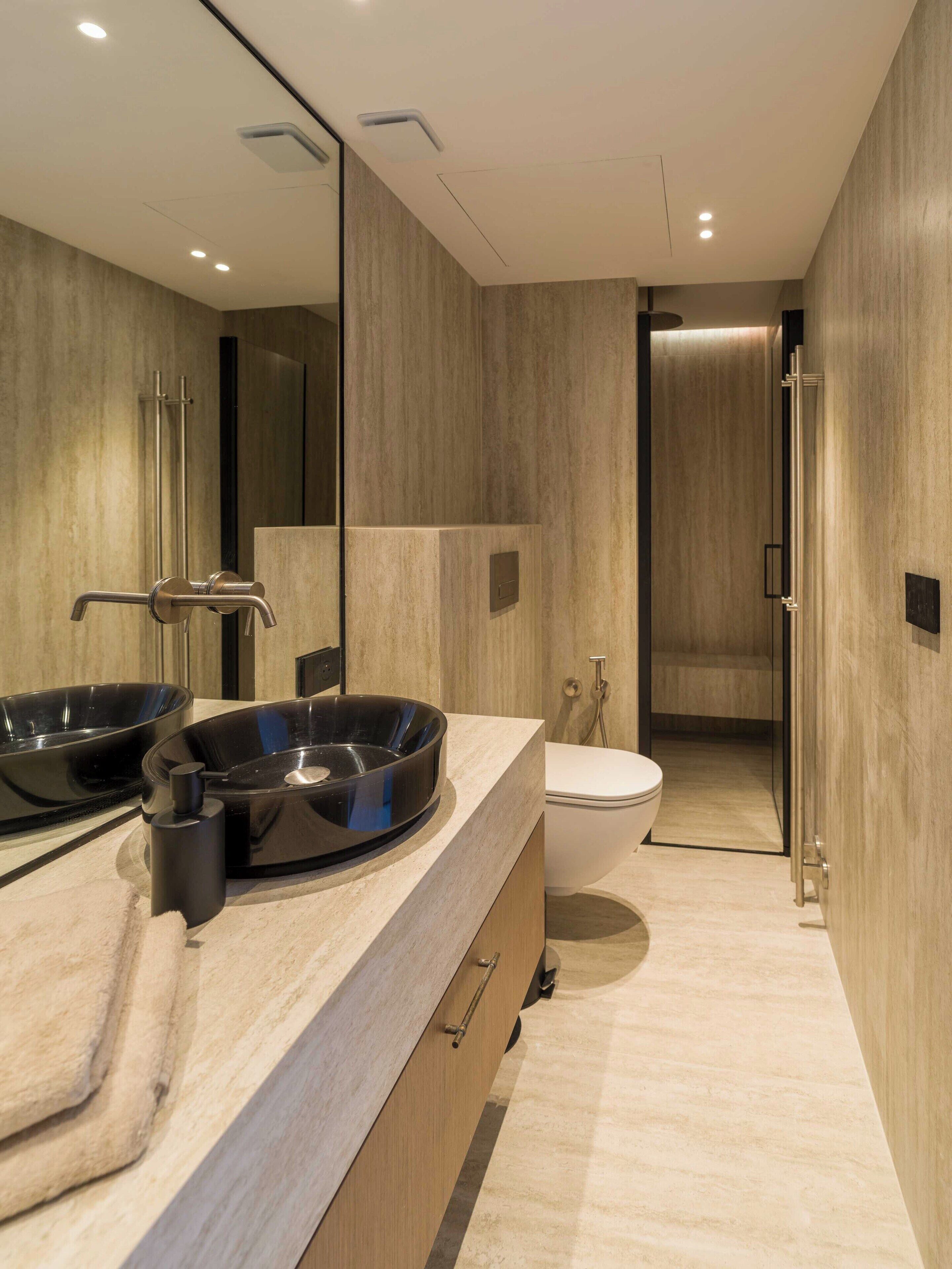 Un baño moderno con un espejo grande, un lavabo redondo con una pileta negra, inodoro y zona de ducha.