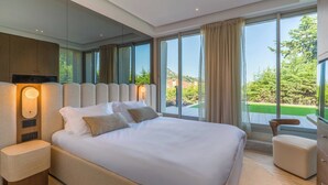A modern bedroom with a large bed, a nightstand, a wooden headboard, and a view of a green landscape through large windows. - High-end Apartment With Spacious Terrace (Villefranche-sur-Mer)