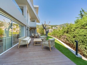 A modern outdoor patio with wicker furniture, a glass door leading to a balcony, and a view of a hillside community. - Design Apt & Spacious Terrace - Villefranche (Villefranche-sur-Mer)