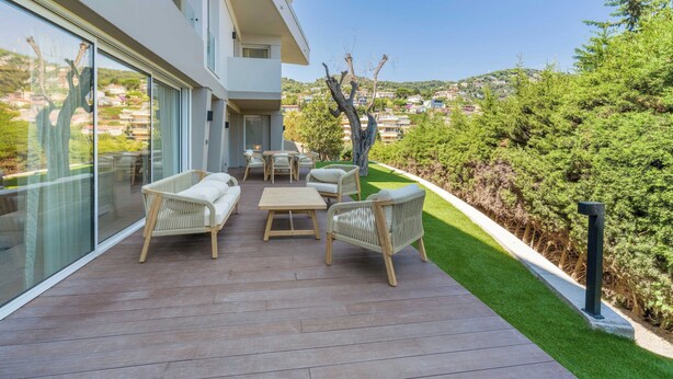 A modern outdoor patio with wicker furniture, a glass door leading to a balcony, and a view of a hillside community. - High-end Apartment With Spacious Terrace (Villefranche-sur-Mer)