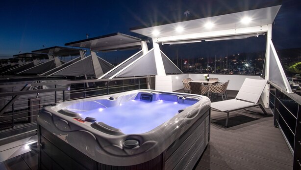 Terraza en la azotea con hidromasaje, mobiliario exterior y vista a la ciudad al atardecer.