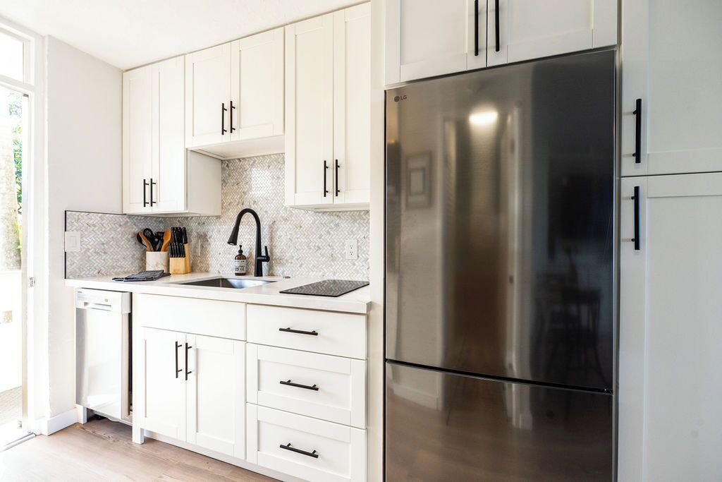 Een moderne keuken met witte kasten, een roestvrijstalen koelkast en een backsplash met een hongaars patroon.